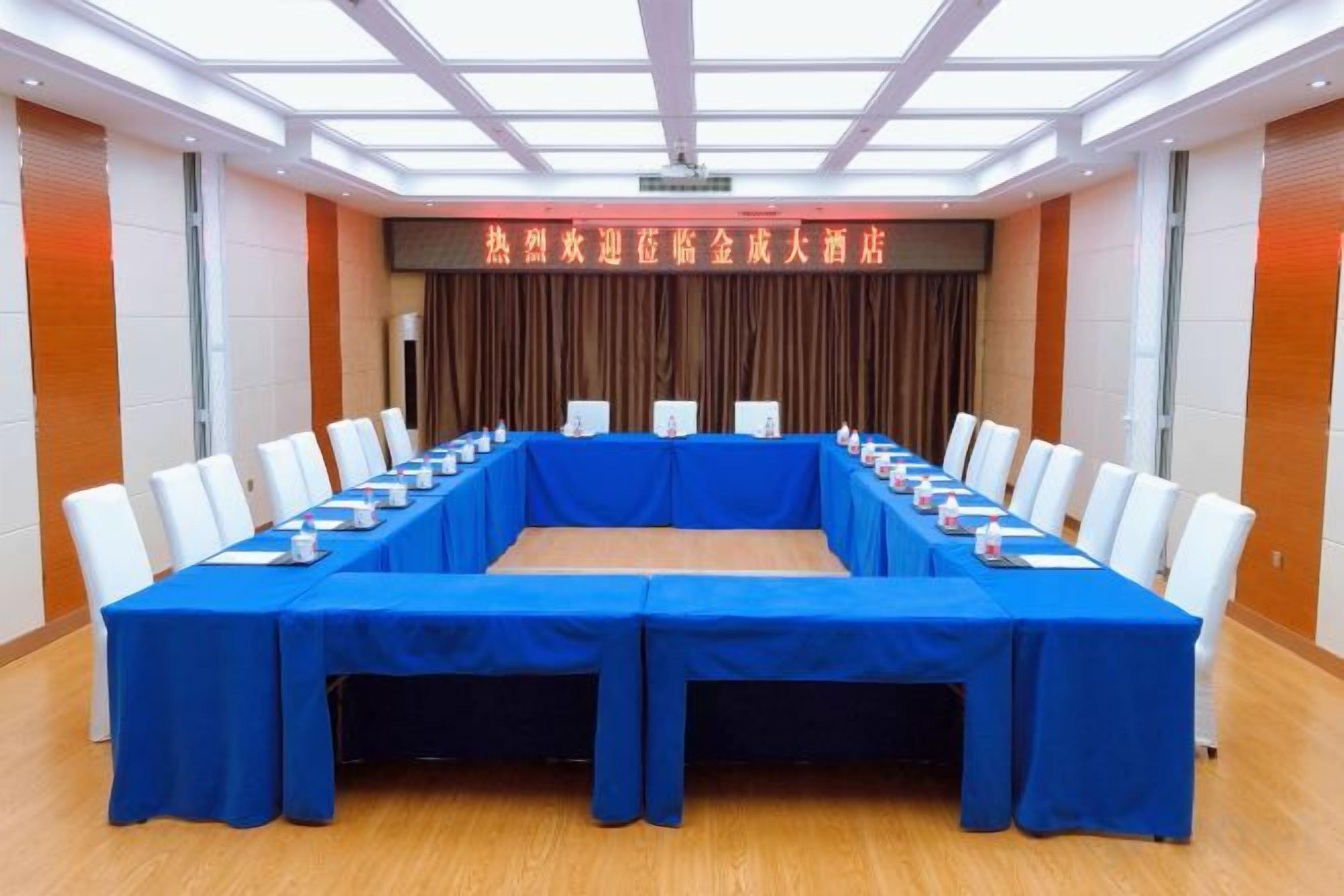 A conference room with a long table, white chairs, and a blue tablecloth.