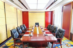Un salón de conferencias con una larga mesa, sillas negras y piso alfombrado.