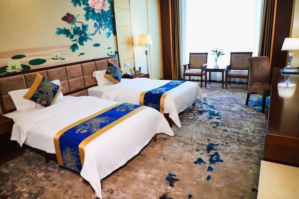 A hotel room with two beds, a large floral mural, a carpeted floor, and a view of the outdoors.