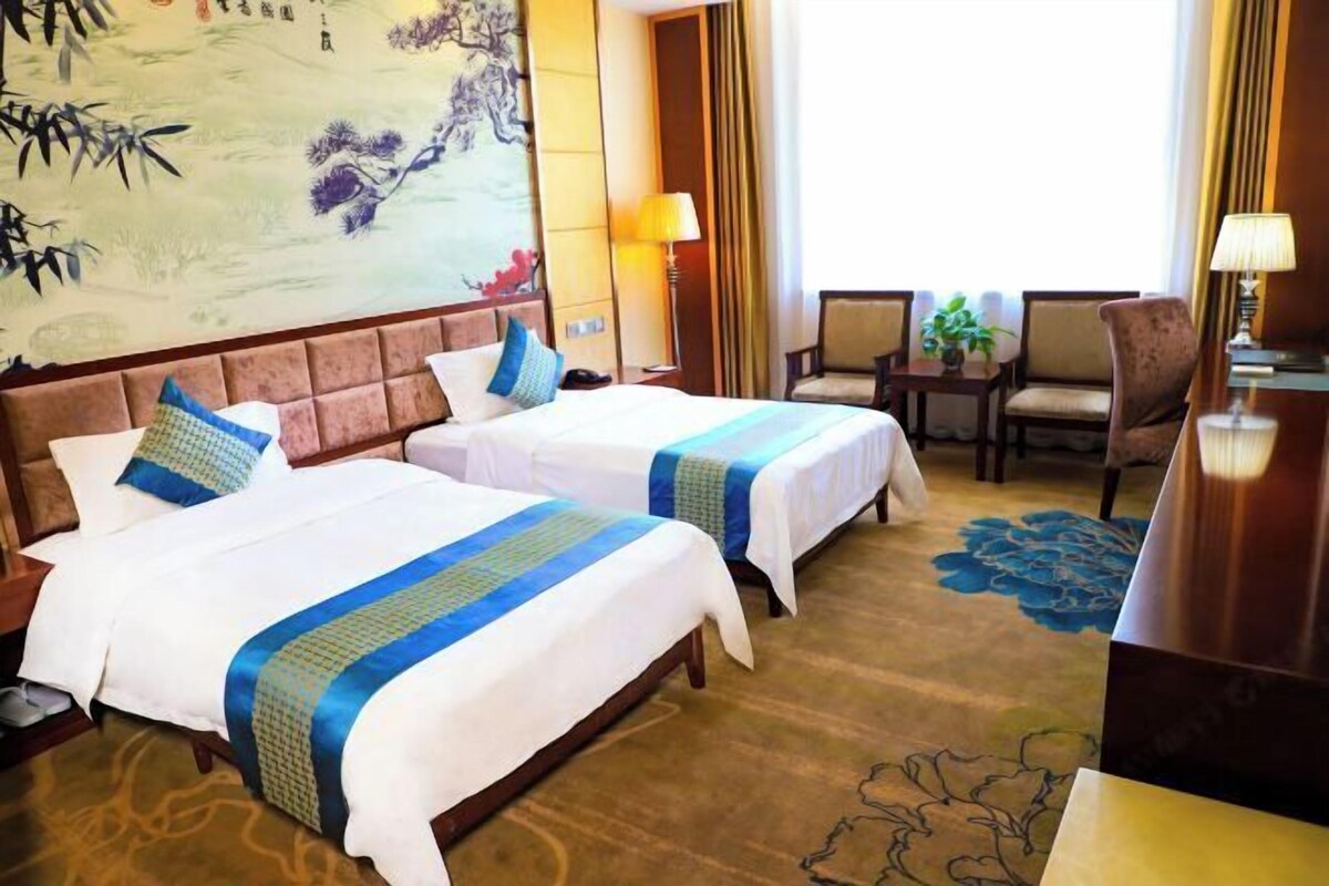 A hotel room with two beds, a large wall painting, a desk, and a chair.