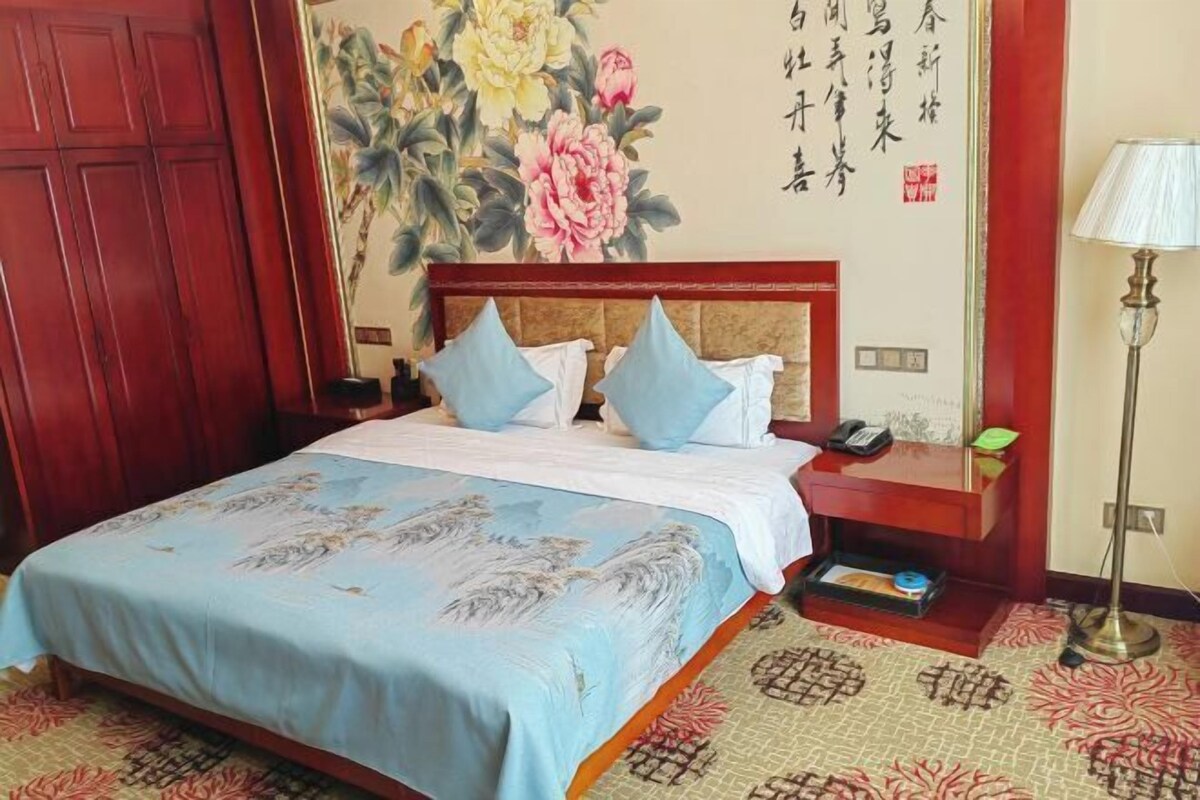 A hotel room with a bed, a nightstand, a lamp, and a wall with floral artwork.