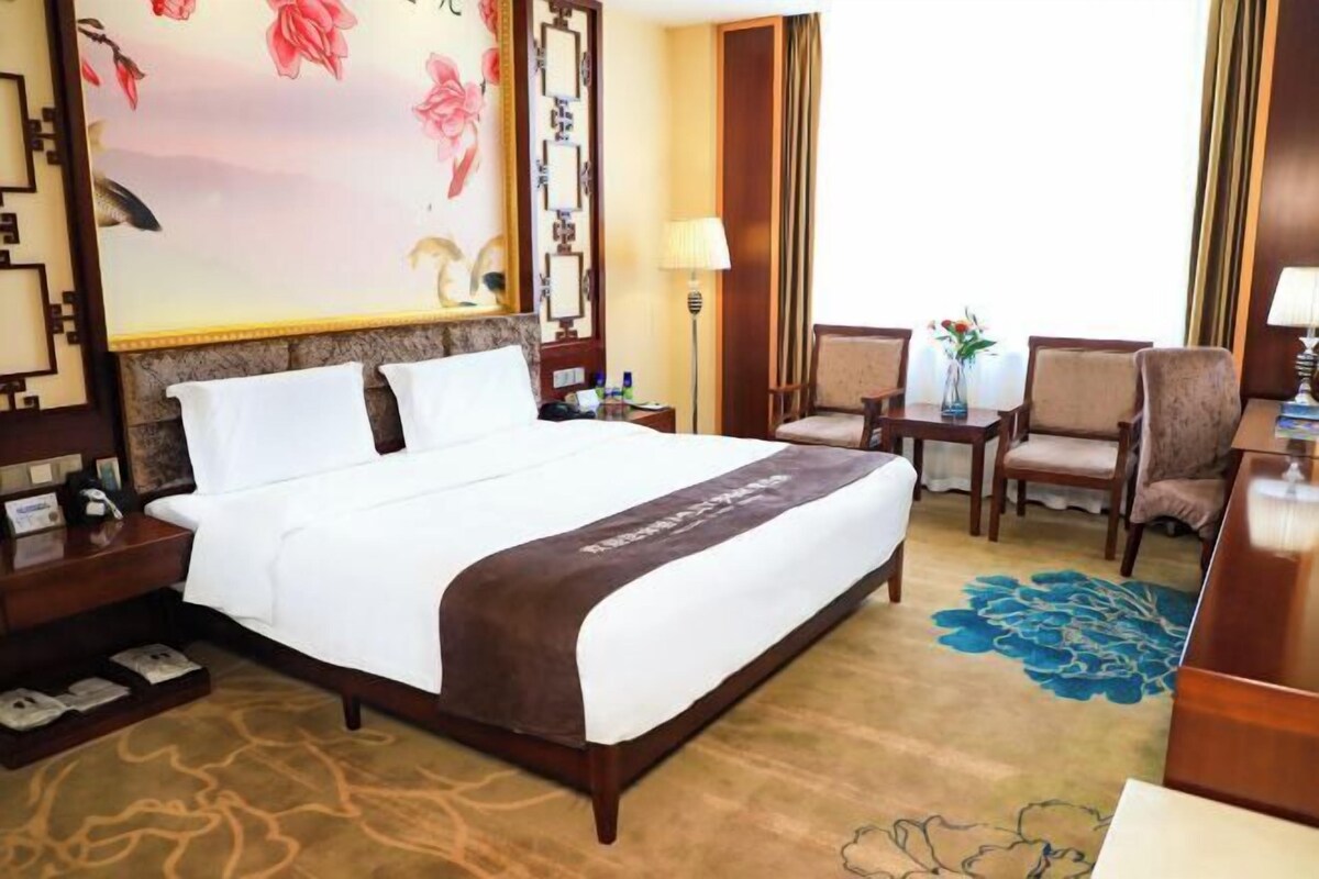 A hotel room with a large bed, two bedside tables, a desk, and a chair.