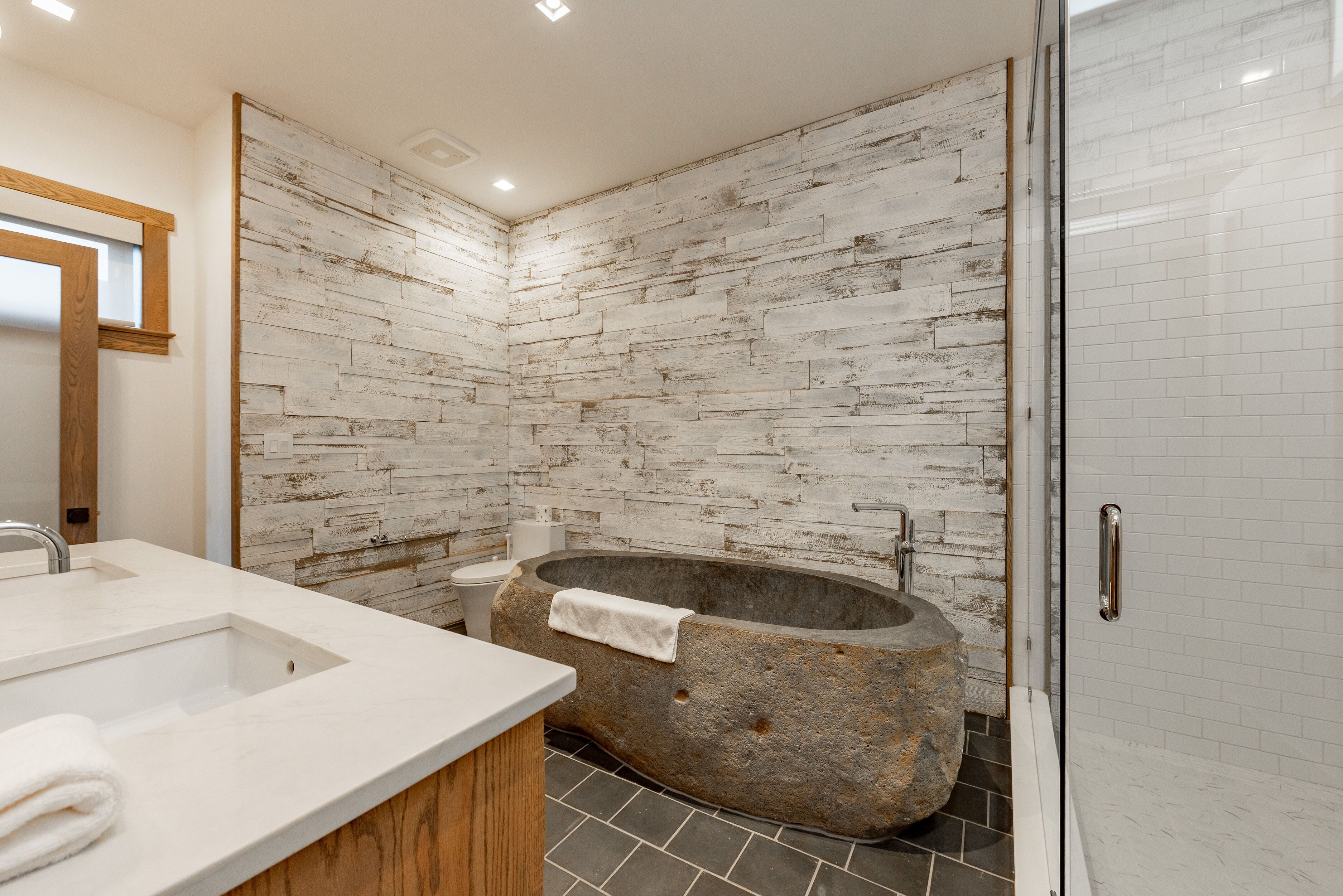 A modern bathroom with a stone bathtub, white tiled walls, and a wooden vanity.