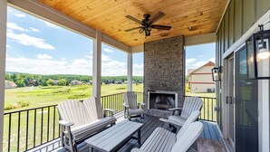 Een overdekt terras met Adirondack-stoelen, een tafel en een stenen openhaard.