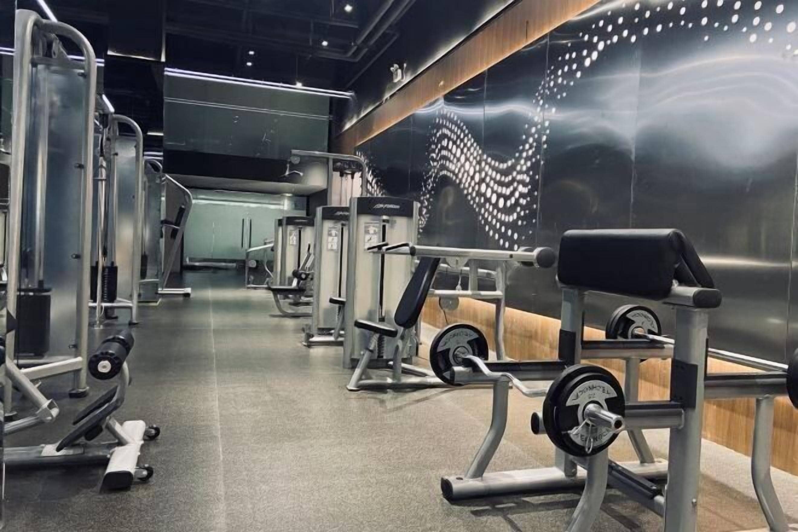 Un gimnasio con diversos equipos de ejercicio, incluyendo máquinas de pesas y pesas libres, dispuesto en un espacio amplio.
