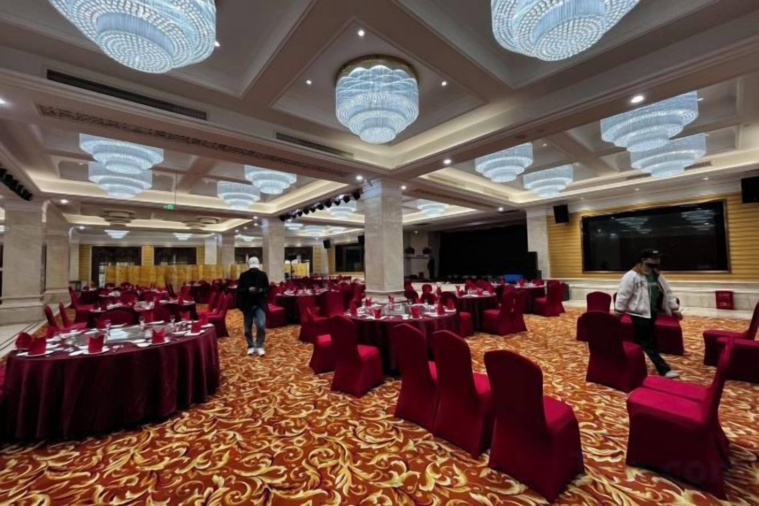 Un salón de banquetes con mesas redondas, sillas rojas y candelabros.