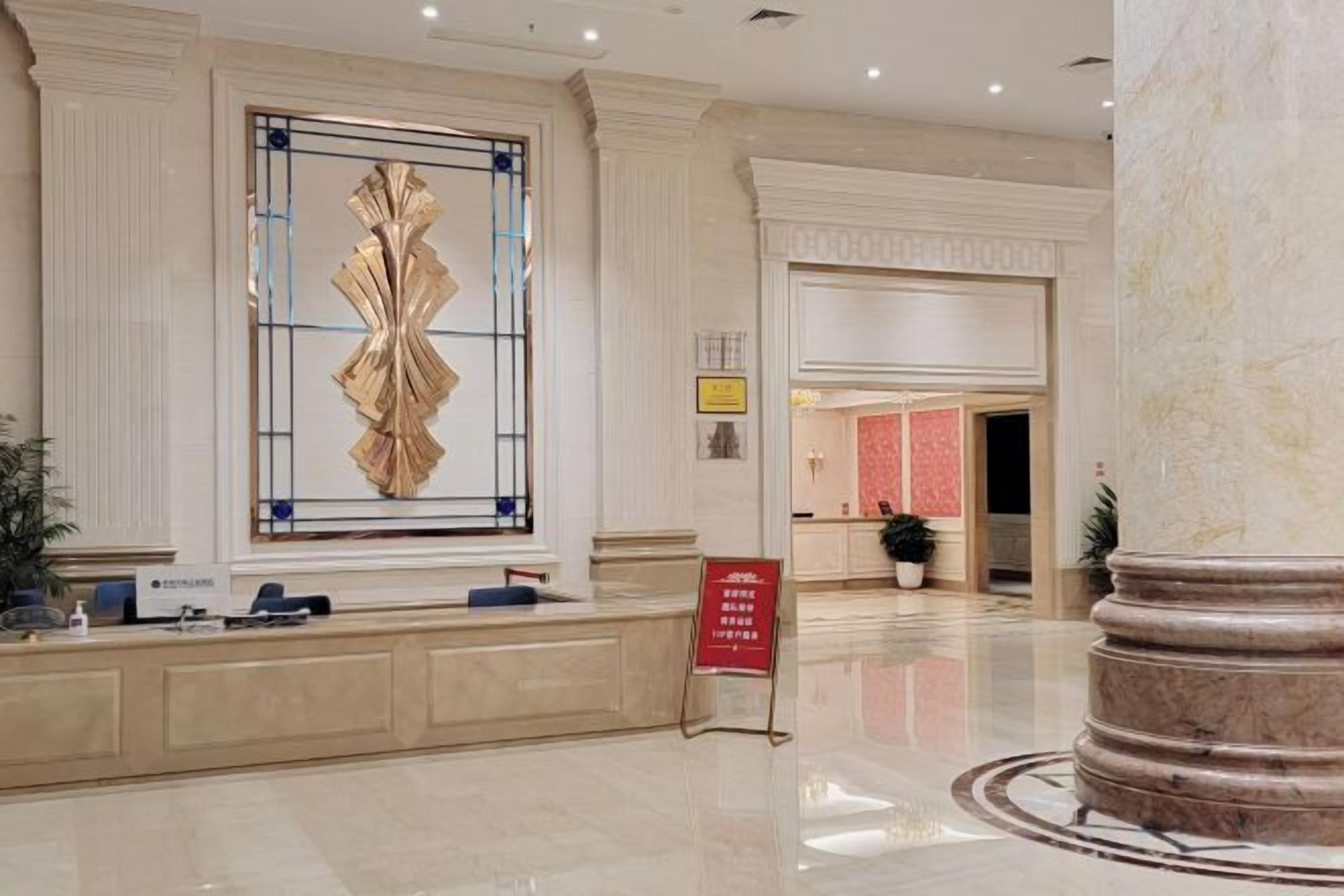 Un vestíbulo de hotel con una recepción, un ventanal decorativo grande y una columna de mármol.