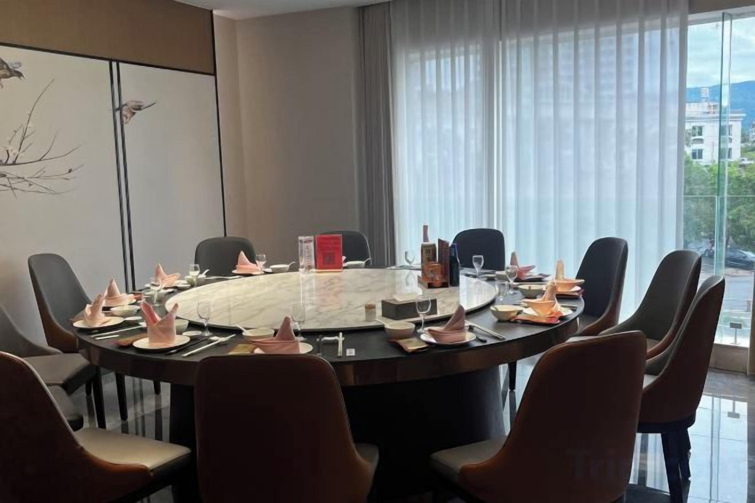 Un salón de conferencias con una mesa redonda, sillas y vistas a la ciudad a través de amplios ventanales.