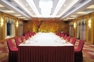 A conference room with a long table set for a meeting, surrounded by chairs, with a decorative wall mural in the background.