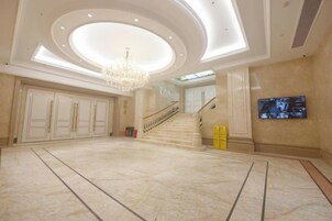 Un hall espacioso con una gran escalera, un candelabro y un televisor de pantalla plana en la pared.