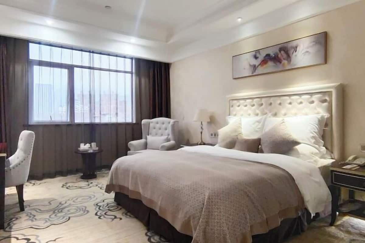 Ein Hotelzimmer mit einem großen Bett, einem Sessel, einem Nachttisch mit Lampe und einem fenster mit Vorhängen.