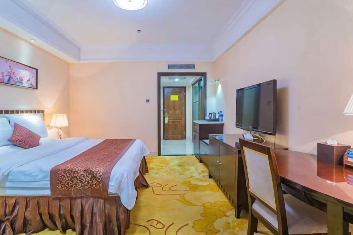 Ein Hotelzimmer mit Bett, Schreibtisch, Fernseher und einem durchgegangenen Tür sichtbaren Badezimmer.