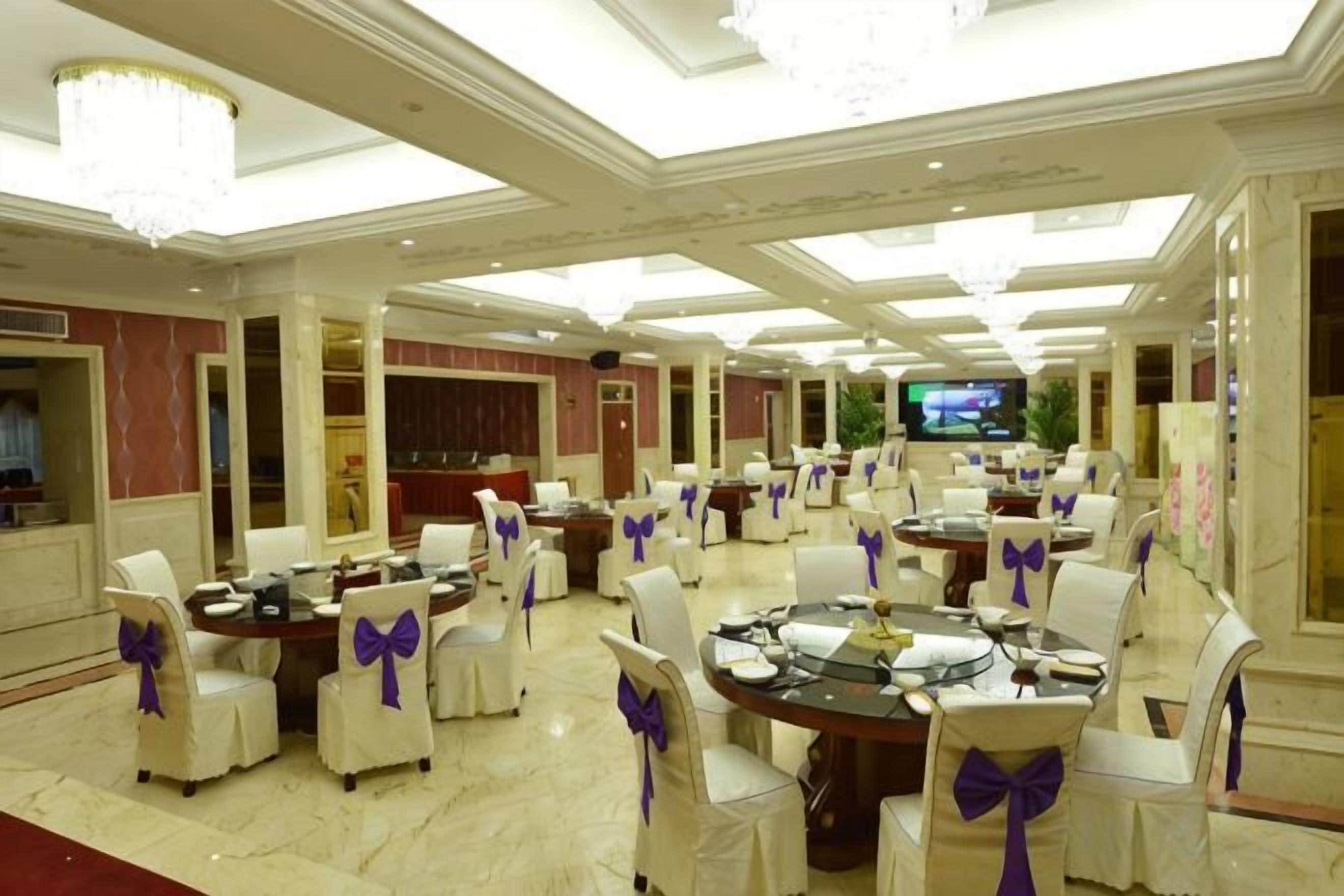 A banquet hall with round tables, chairs, and a television screen.