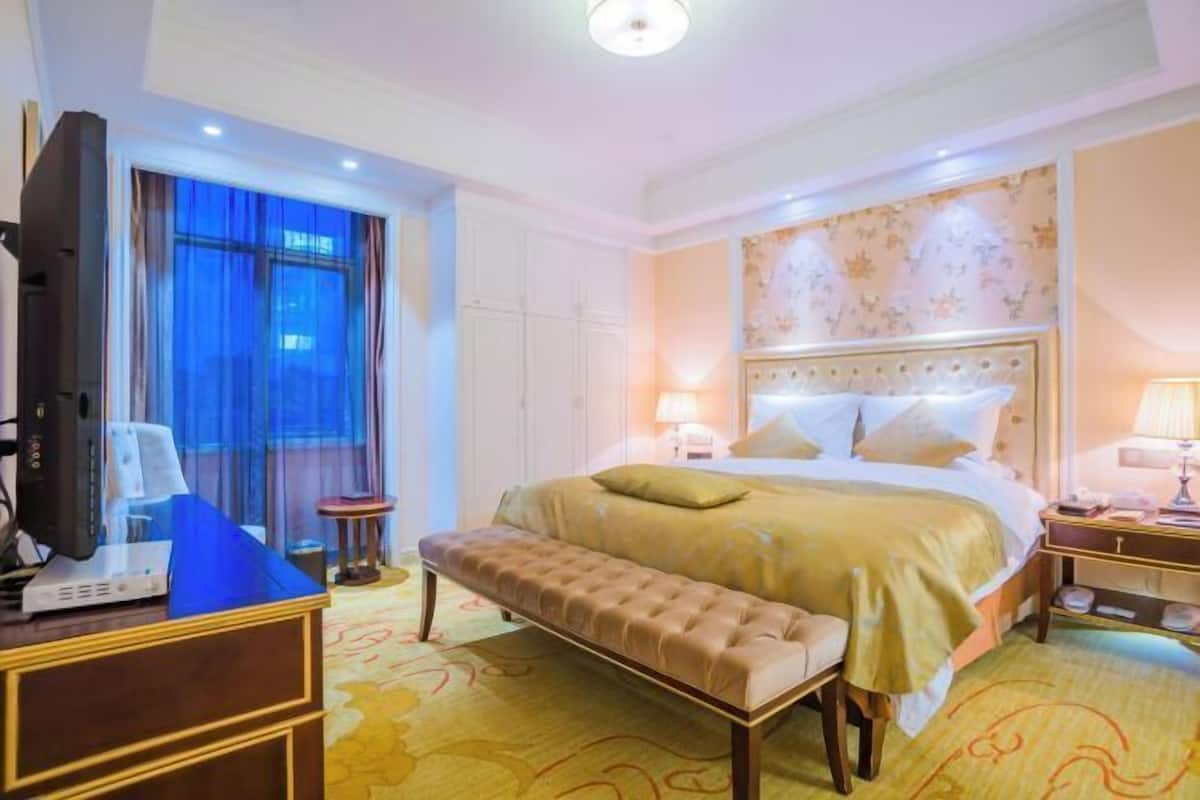 Ein Hotelzimmer mit einem großen Bett, einer Bank, einem Fernseher und einem Schreibtisch mit Lampe.