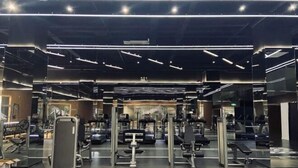Un gimnasio con paredes de espejo, diverso equipo de ejercicio e iluminación en el techo.