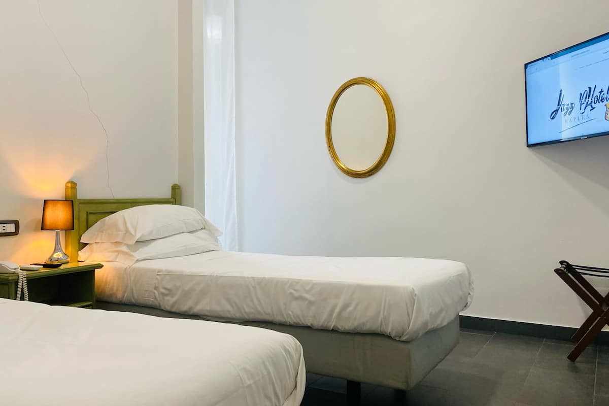 Une chambre d’hôtel avec deux lits simples, une table de chevet avec une lampe, une prise de courant et un téléviseur affichant le nom de l’hôtel.