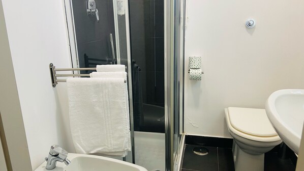 A bathroom with a glass shower enclosure, a white sink, and a toilet. - Jazz Hotel (Naples)