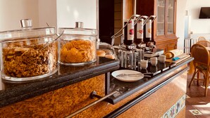 A breakfast bar with cereal and granola containers, a coffee machine, and a wooden cabinet. - Jazz Hotel (Naples)