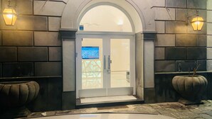 A hotel entrance with a glass door, stone walls, and two wall-mounted lights. - Jazz Hotel (Naples)