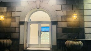 A hotel entrance with a stone facade, a glass door, and two wall-mounted lamps. - Jazz Hotel (Naples)