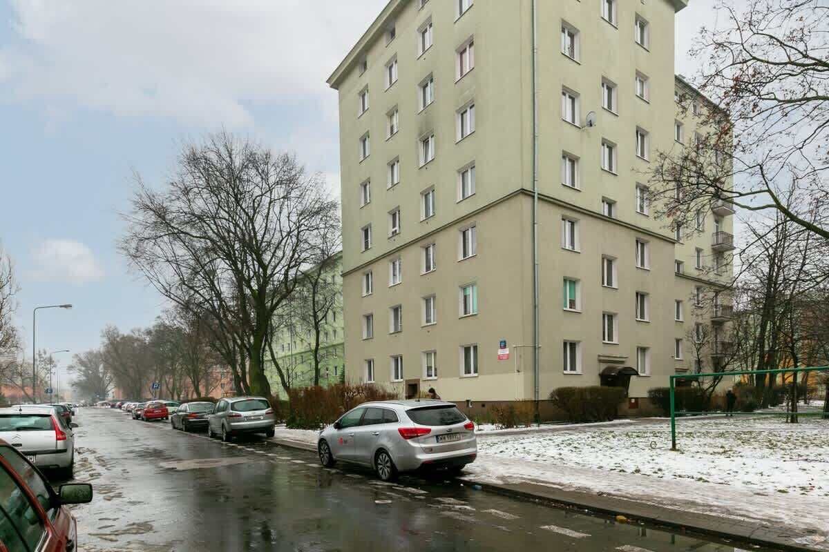 A multi-story residential building with a row of parked cars along the street.