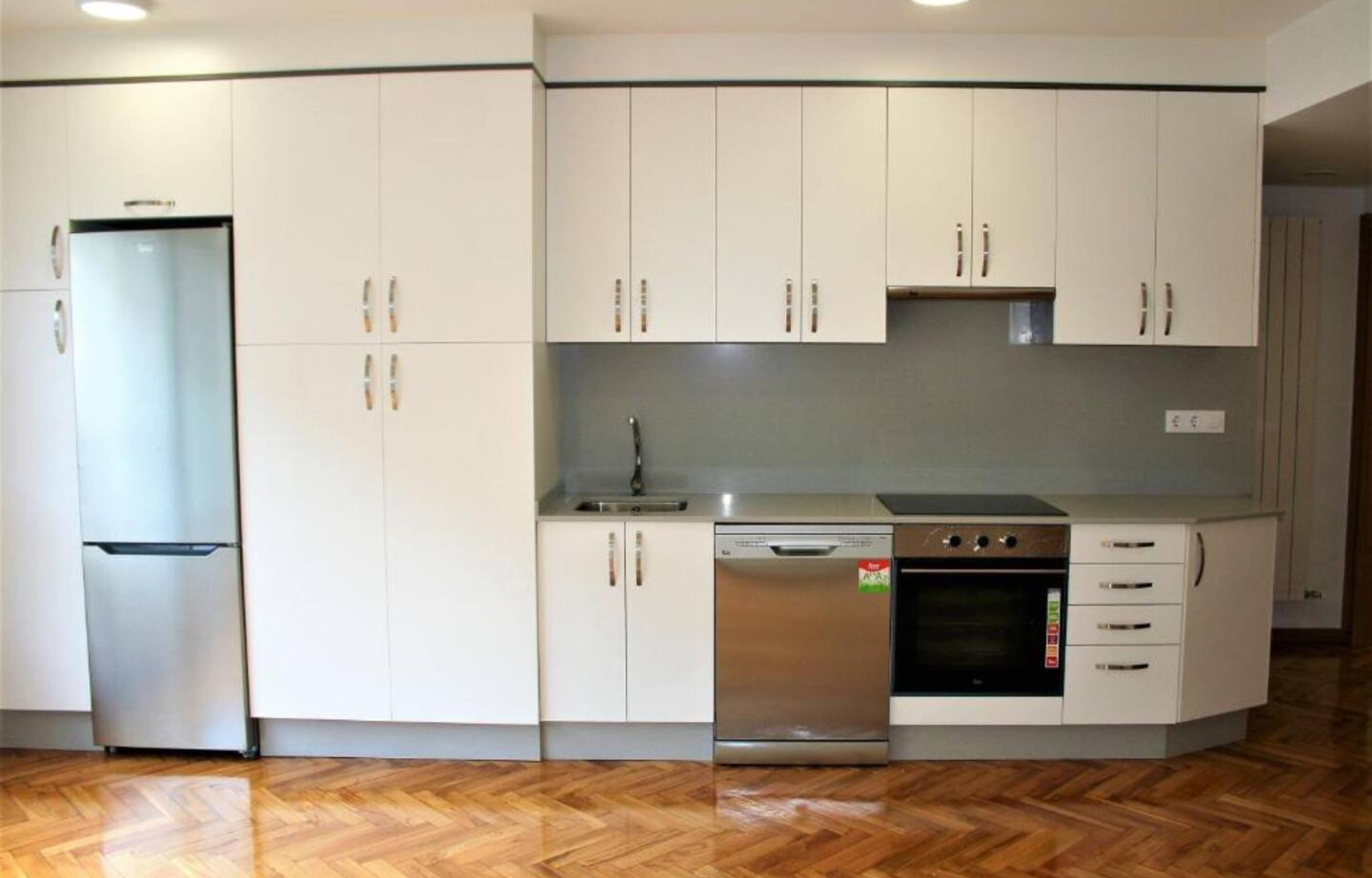 A kitchen with white cabinets, a stainless steel refrigerator, a dishwasher, and an oven.