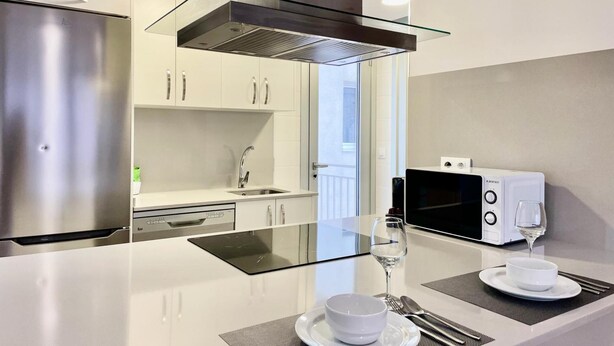 Une cuisine moderne dotée d’appareils électroménagers en acier inoxydable, d’un îlot central en verre et d’un coin repas agrémenté d’un verre à vin et d’un saladier en verre.