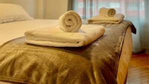 Une chambre d’hôtel avec un lit bien fait, un coussin décoratif doré et une serviette roulée posée sur le lit.