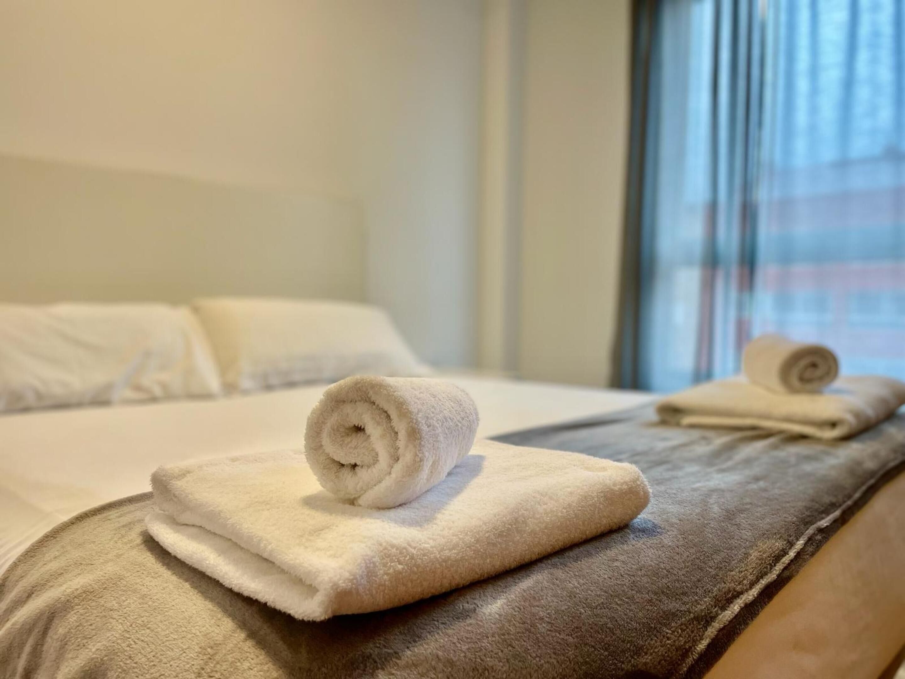 A hotel room with a neatly made bed, a window with blinds, and a view of a building outside.