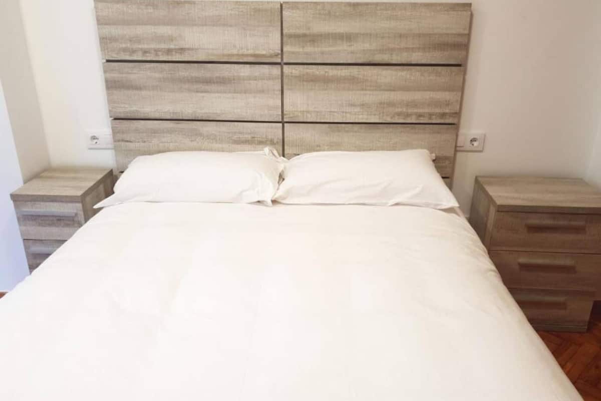 A bed with a wooden headboard, two bedside tables, and a drawer unit.