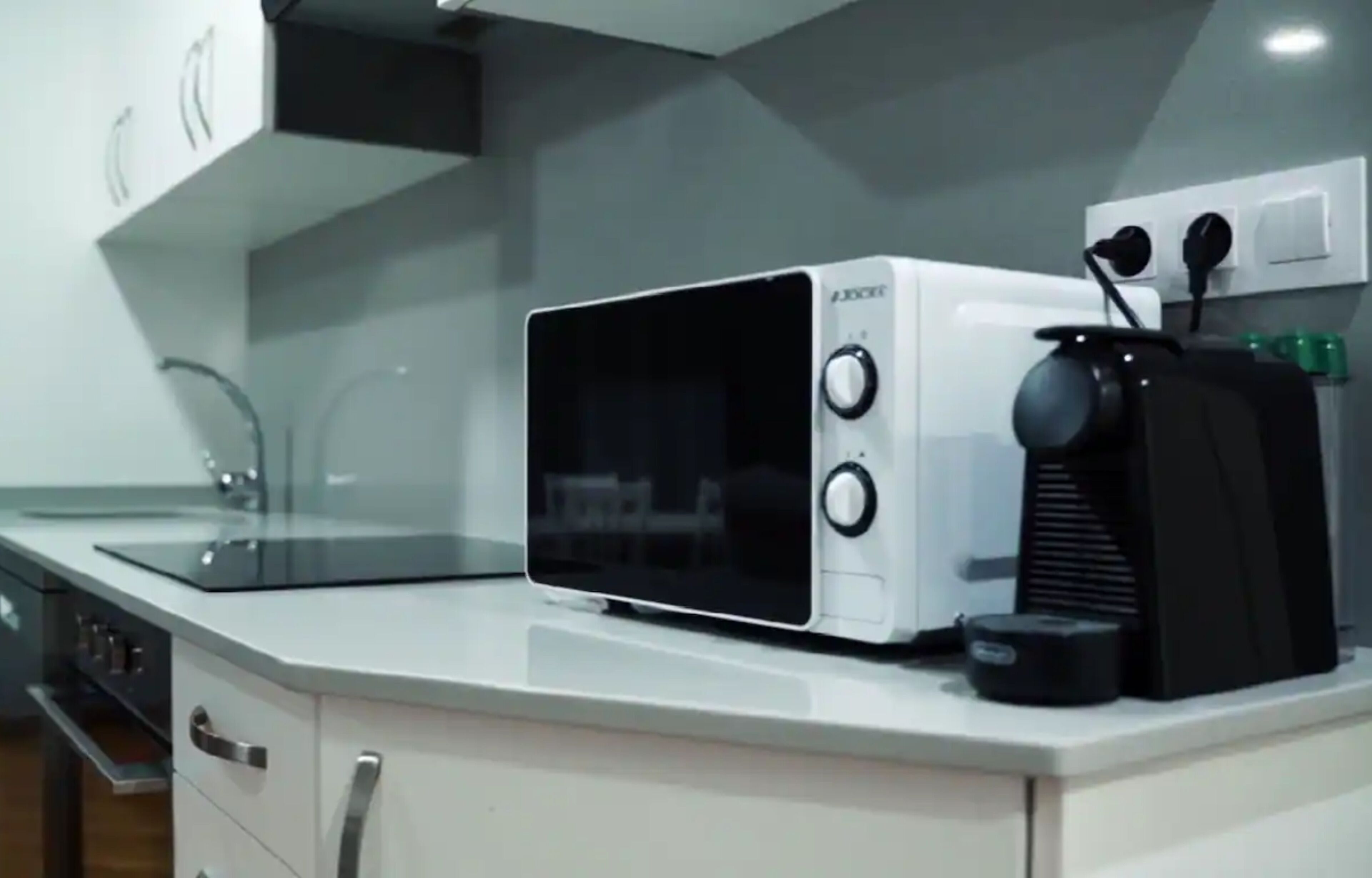 A compact kitchen with a microwave, a coffee maker, and a kettle on the counter.