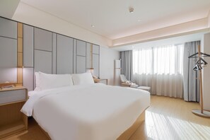 Moderni hotellihuone, jossa on suuri sänky, yöpöydät, työpöytä, tuoli, lamppu ja ikkuna, jossa on verhot.