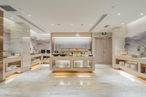 Hotellihuone, jossa on suuri peili, monipuolinen buffetpöytä ja puinen ovi.