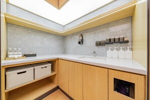 Moderni kylpyhuone, jossa on valkoinen työtaso, puukaapit ja sisäänrakennettu hylly, jossa on hygieniatuotteita.