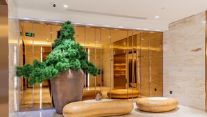 Eine moderne Lobby mit einem großen, künstlichen Weihnachtsbaum, einer Holzbank und einem Marmorboden.