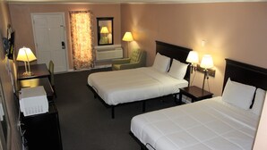 Una habitación de hotel con dos camas individuales, un escritorio con lámpara, una silla y una mesita con lámpara.