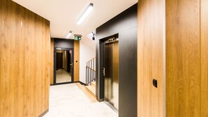 A modern hallway with wooden paneling, a visible elevator, and a staircase leading to another floor. - Apartamenty Bema od WroclawApartament-pl (Wroclaw)