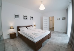 A bedroom with a wooden bed, bedside lamps, a nightstand, and a door leading to another room. - Apartamenty Bema od WroclawApartament-pl (Wroclaw)