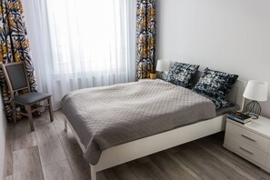 A neatly arranged bedroom with a bed, bedside tables, a chair, and a small table with a lamp. - Apartamenty Bema od WroclawApartament-pl (Wroclaw)