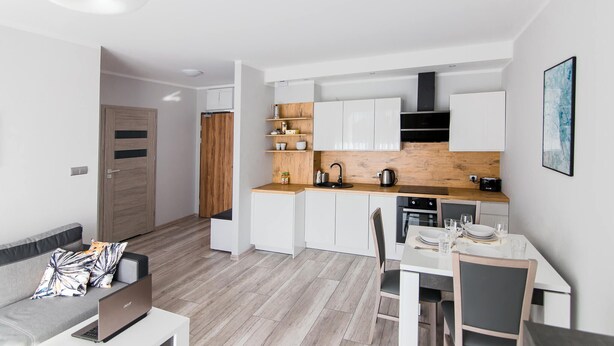A modern kitchen with white cabinets, a wooden countertop, and a dining area with a table and chairs. - Apartamenty Bema od WroclawApartament-pl (Wroclaw)
