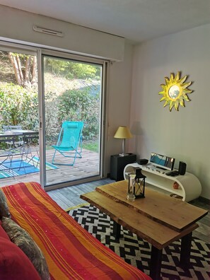 A modern living room with a sliding glass door leading to an outdoor area, a wooden coffee table, a colorful striped rug, a sofa, and a wall-mounted sun decoration.