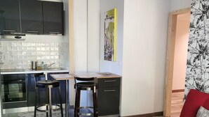 A compact living space with a kitchenette, a dining area with a table and chairs, a bed with a red and orange striped blanket, and a patterned wall hanging. - Biarritz charming two-room apartment with garden and parking! (Biarritz)