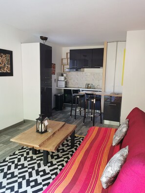 A compact living space with a kitchenette, a dining area, and a sofa with cushions.