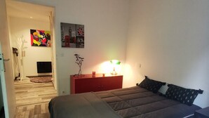 A bedroom with a bed, a nightstand, a lamp, and a door leading to another room. - Biarritz charming two-room apartment with garden and parking! (Biarritz)