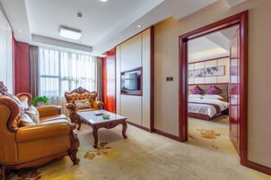 Habitación de hotel con sofá, sillón, televisión y cama con cabecero rojo.