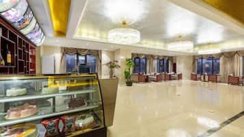 A hotel lobby with a glass display case of desserts, a chandelier, and a seating area with red upholstered chairs.