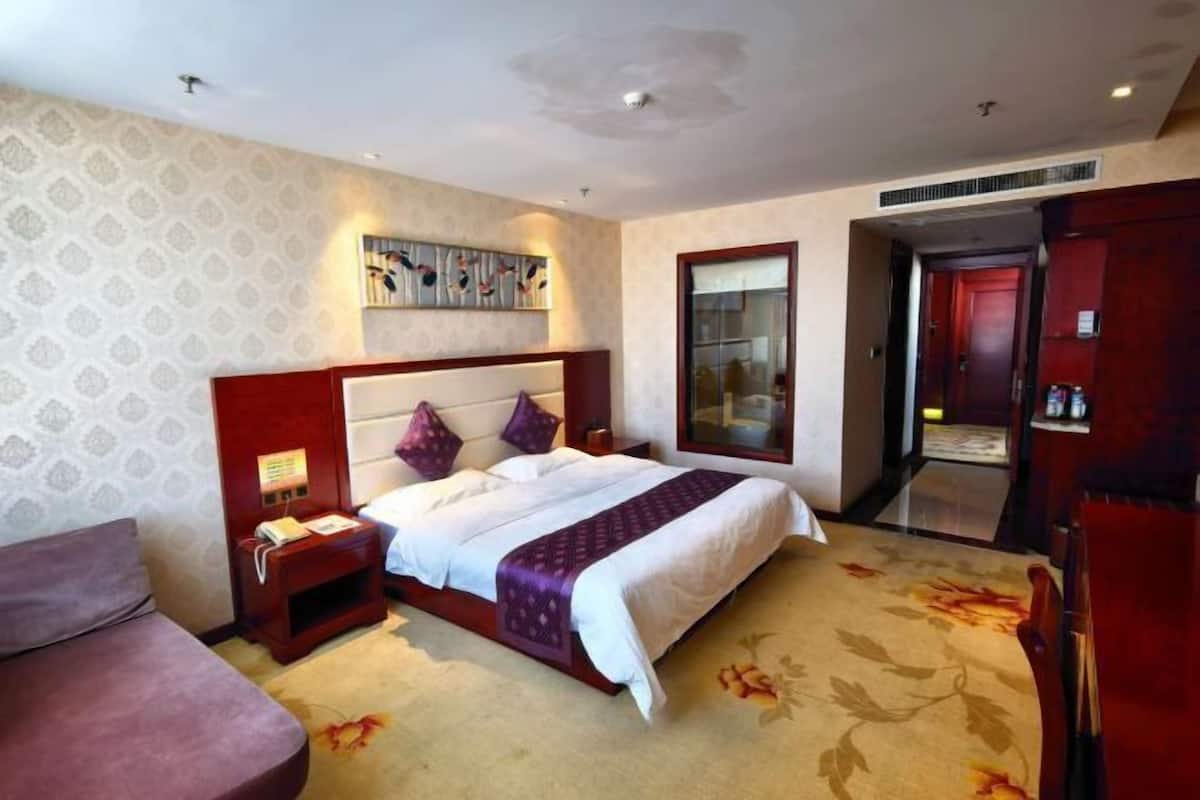 A hotel room with a large bed, a nightstand, a desk, a chair, and a large mirror.
