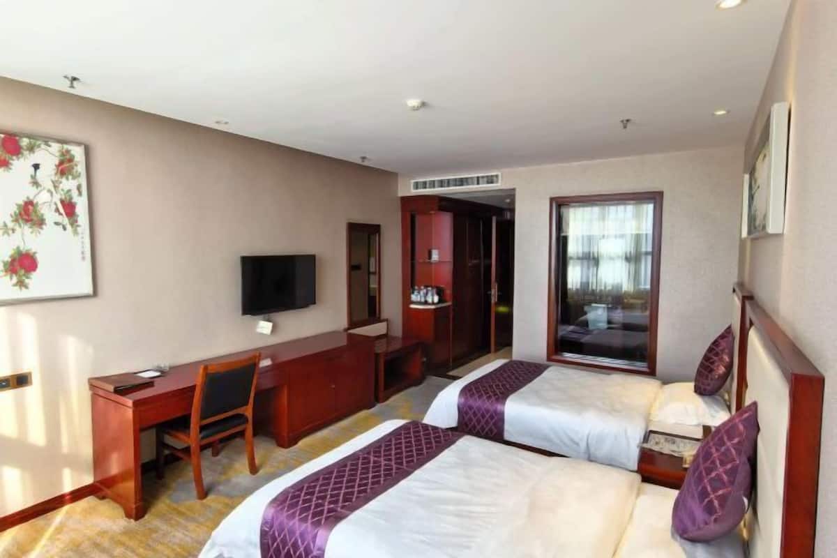 A hotel room with two beds, a desk, a chair, a TV, and a window.