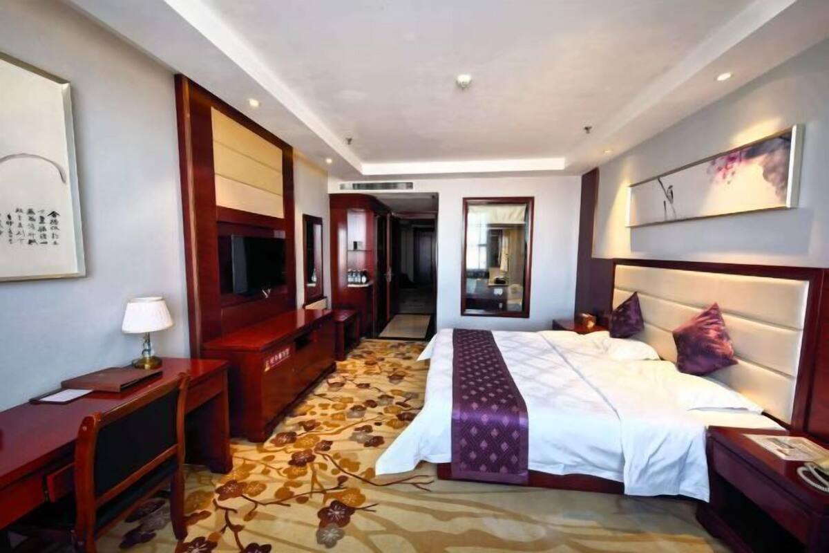 A hotel room with a bed, a desk, a television, and a mirror.