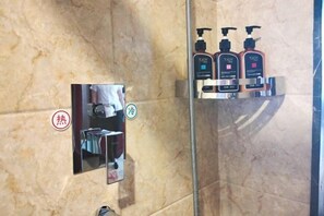 Un baño con pared de mármol, un espejo, un perchero para toallas y tres botellas de artículos de aseo.
